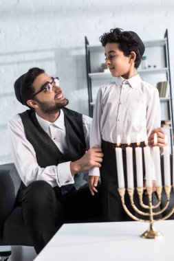smiling jewish father looking at cute son in apartment  clipart
