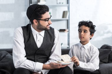 Gülümseyen Yahudi baba tabak tutuyor ve oğlu Matza 'yı evine alıyor. 