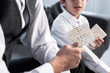 cropped view of jewish father and son holding matza in apartment  clipart