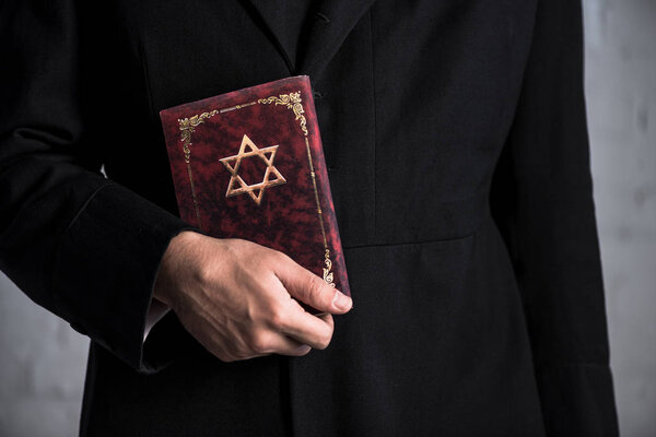 cropped view of young jewish man holding tanakh 