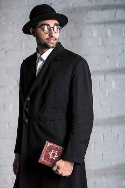 handsome and smiling jewish man in glasses holding tanakh 