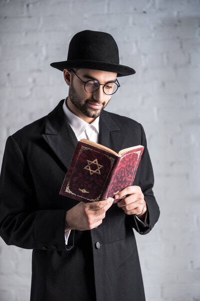 handsome and smiling jewish man in glasses reading tanakh 