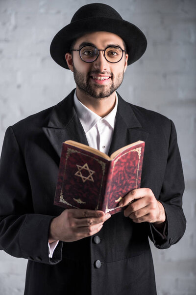 handsome and smiling jewish man in glasses holding tanakh 