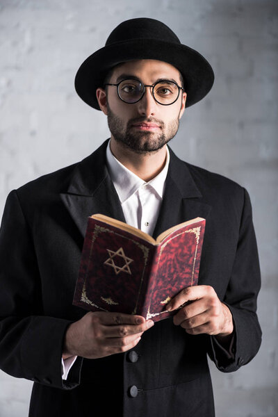 handsome and young jewish man in glasses holding tanakh 