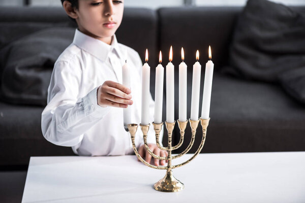 обрезанный вид симпатичного еврейского мальчика в рубашке, держащего свечу
 