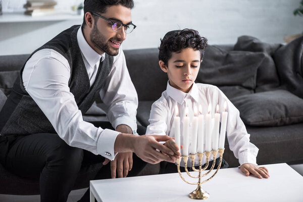 улыбающиеся еврейский отец и сын держа свечу в квартире
 