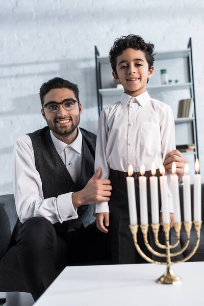 улыбающиеся еврейский отец и сын смотрит в камеру в квартире
 
