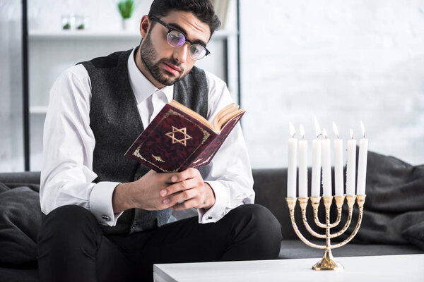 красивый еврей в очках, читающий танах в квартире
 