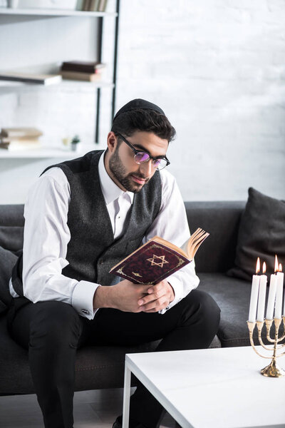 handsome jewish man in glasses reading tanakh in apartment 