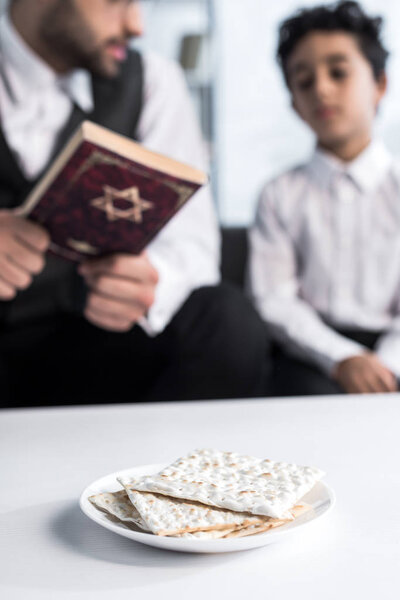 selective focus of matza on plate and jewish father and son on background 