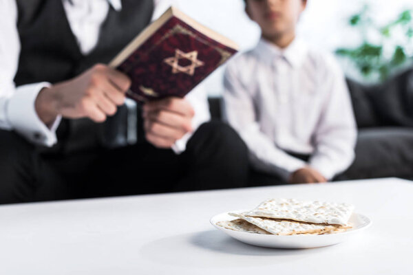 selective focus of matza on plate and jewish father and son on background 