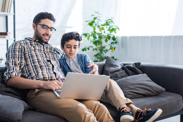 smiling jewish father and son using laptop in apartment 