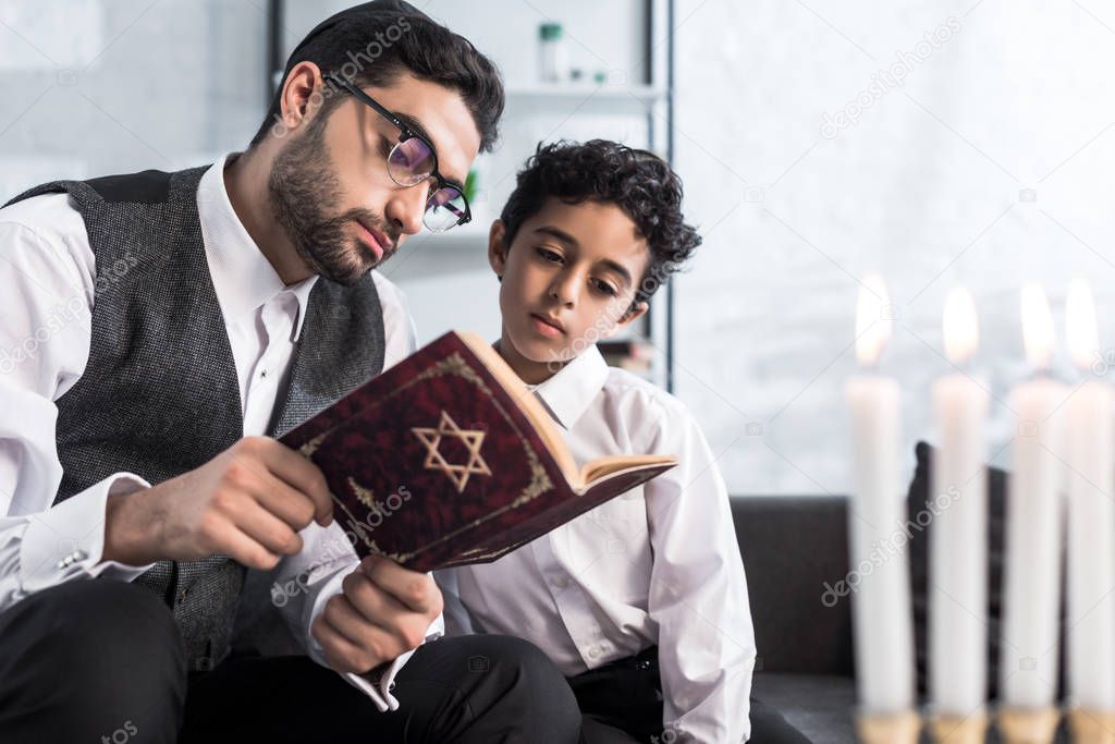 handsome jewish father and son reading tanakh in apartment 