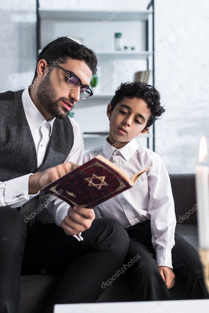 handsome jewish father and son reading tanakh in apartment 