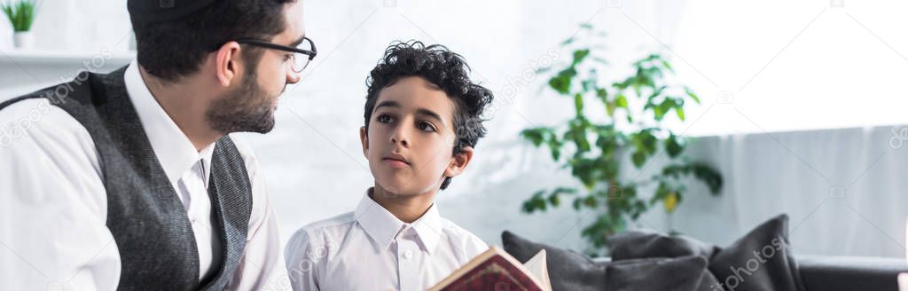 panoramic shot of jewish father and son talking and holding tanakh in apartment 