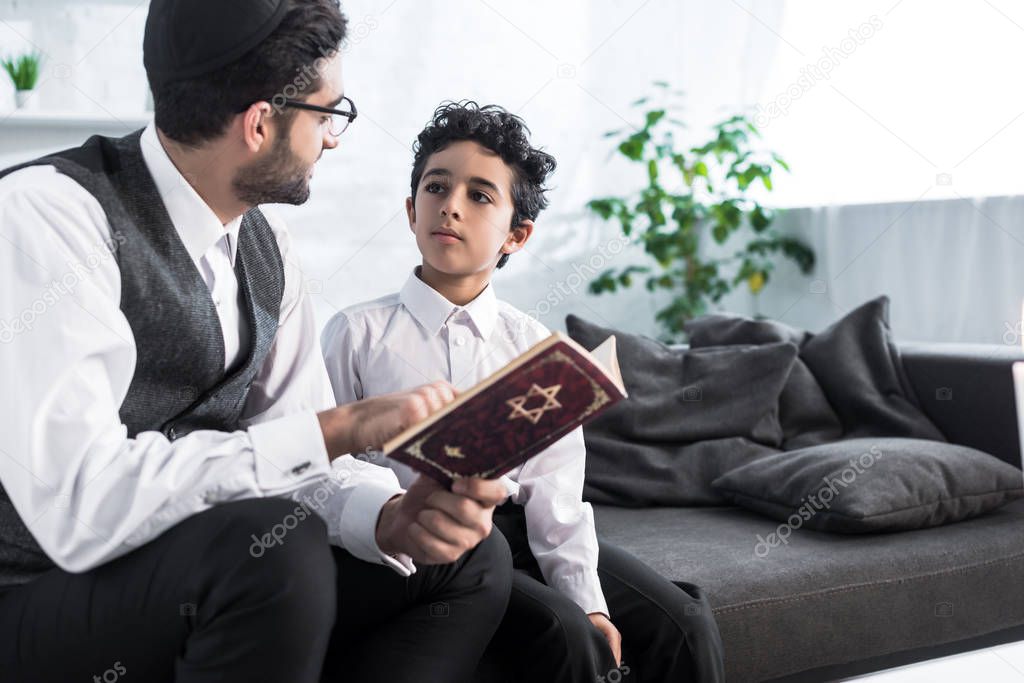 jewish father and son talking and holding tanakh in apartment 