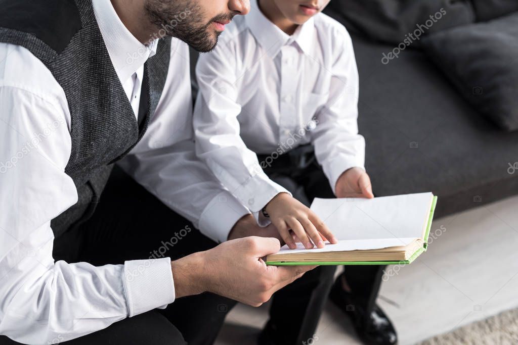 cropped view of jewish father and son reading book in apartment 