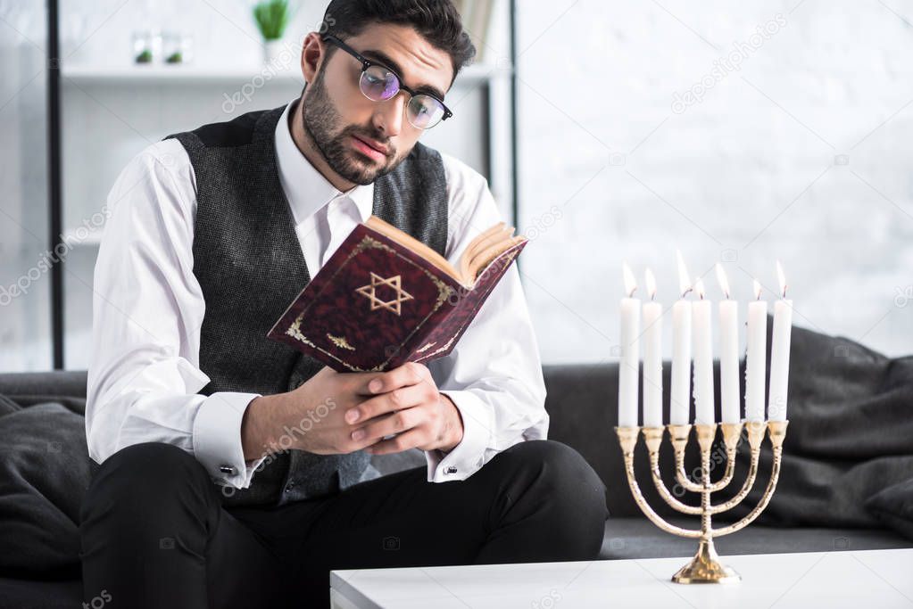 handsome jewish man in glasses reading tanakh in apartment 