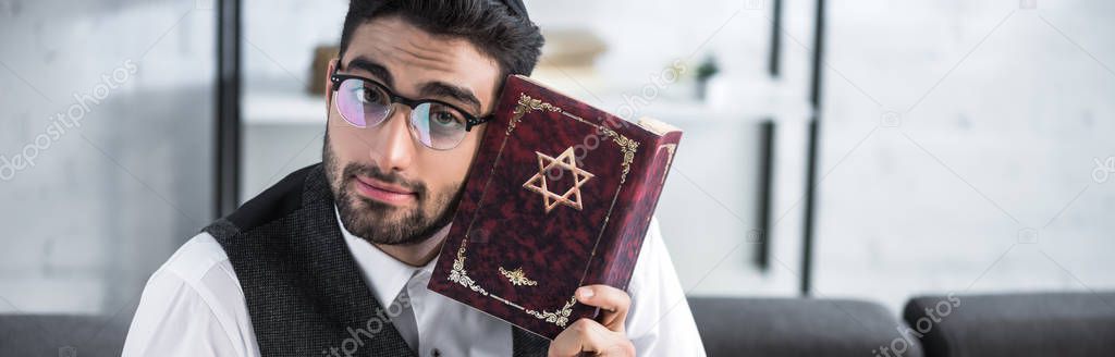 panoramic shot of handsome jewish man in glasses holding tanakh 