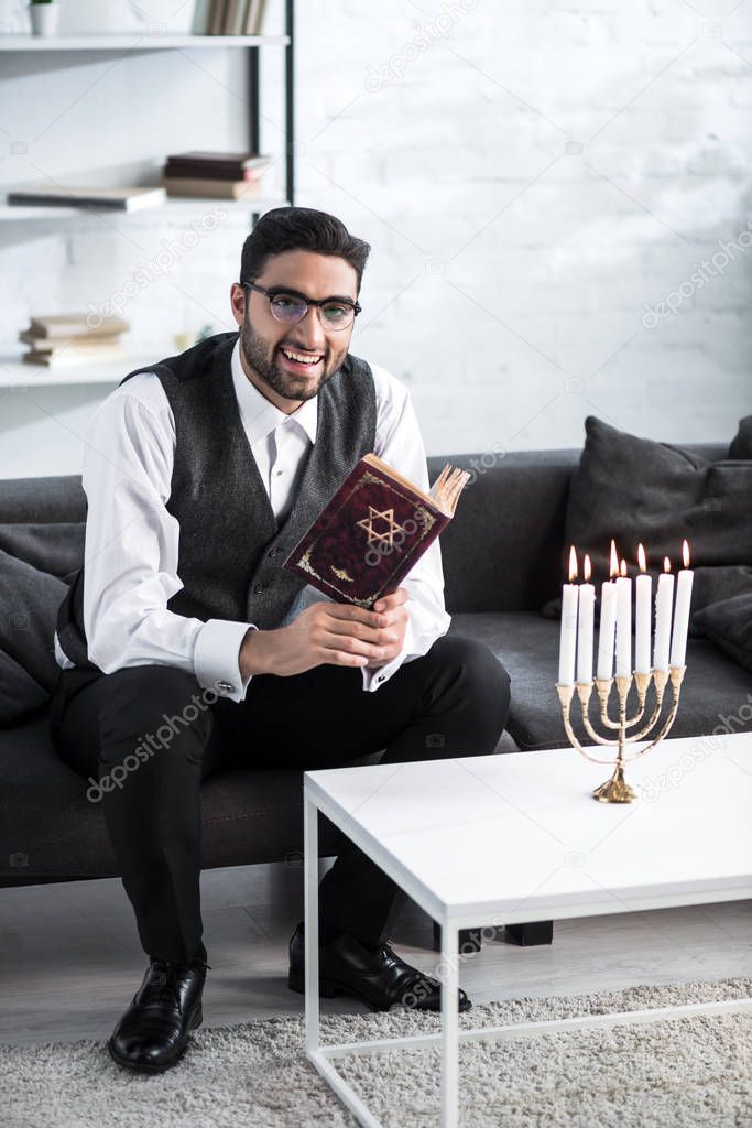 handsome and smiling jewish man in glasses holding tanakh 