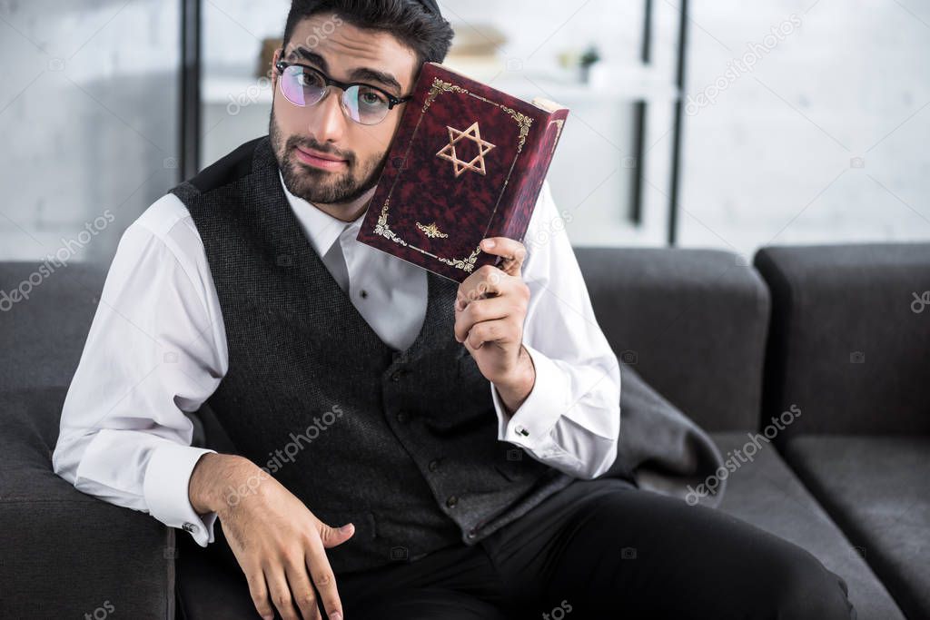 handsome jewish man in glasses holding tanakh and looking at camera 