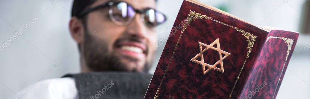 panoramic shot of smiling jewish man in glasses reading tanakh 