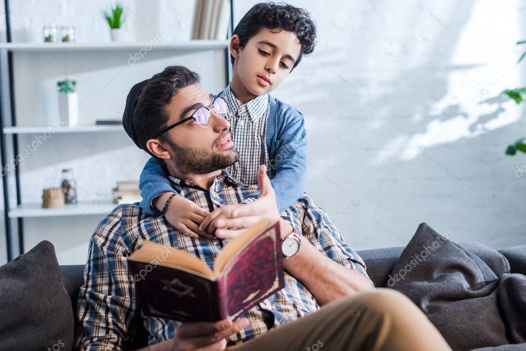 jewish father holding tanakh and talking with son in apartment 