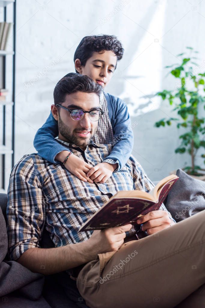 smiling jewish father and son reading tanakh in apartment 