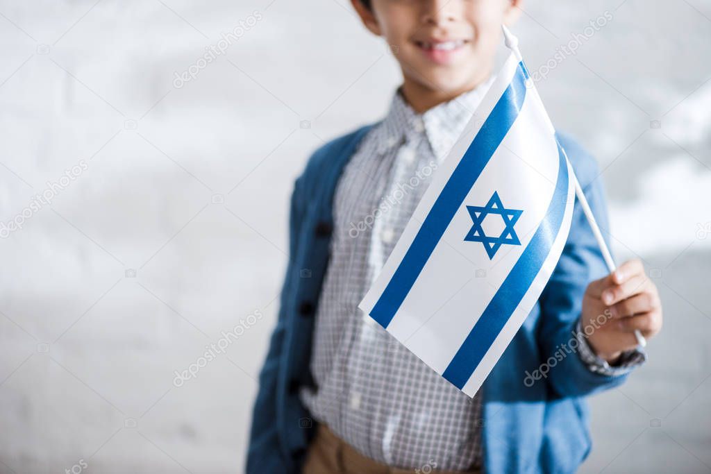 cropped view of smiling jewish boy holding flag of israel 