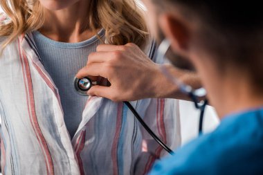 cropped view of doctor holding stethoscope while examining woman  clipart