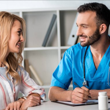 Mutlu sakallı doktorun elinde kalemle klinikteki kadına baktığı seçici odak noktası. 