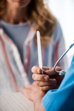 Kadının yanında elinde tıbbi spatula tutan doktor görüntüsü. 