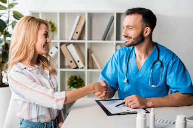happy woman shaking hands with bearded doctor in clinic  clipart