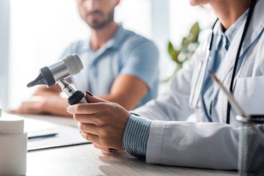 cropped view of doctor holding otoscope near man in clinic 