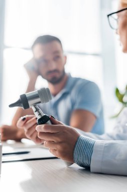 selective focus of doctor in glasses holding otoscope near handsome man in clinic 