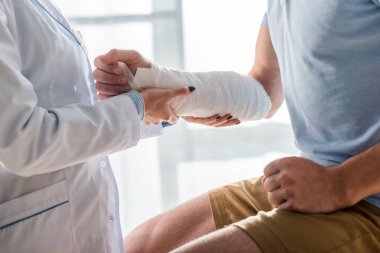 cropped view of orthopedist touching injured arm of man 