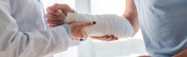 panoramic shot of orthopedist touching injured hand of man  clipart