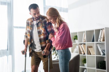 handsome man holding crutches while standing near woman at home 