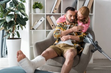 attractive woman hugging injured boyfriend at home 