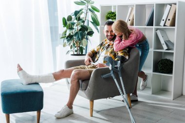 caring woman sitting near cheerful and injured boyfriend 