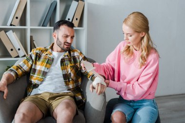 caring woman putting bandage on injured hand of bearded man 