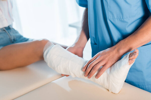 cropped view of orthopedist touching fractured leg of woman 