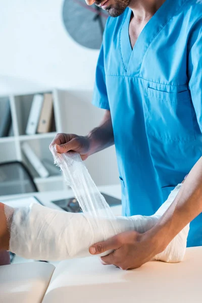 Przycięty Widok Ortopedy Zakładającej Bandaż Złamaną Nogę Kobiety — Zdjęcie stockowe