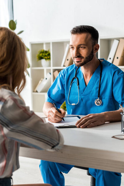selective focus of doctor holding pen and looking at woman 