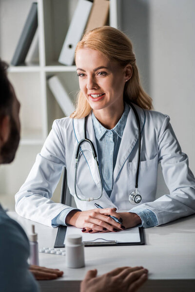 selective focus of cheerful doctor in white coat looking at man 