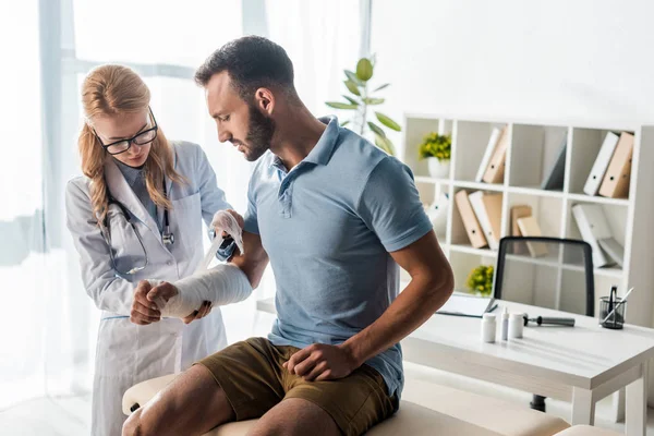 Atractivo Ortopedista Poner Vendaje Mano Lesionada Del Hombre Barbudo — Foto de Stock