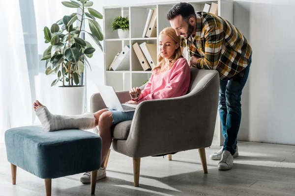 Bel Homme Debout Près Femme Blessée Travaillant Maison Avec Ordinateur — Photo