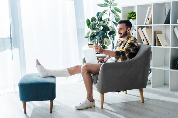 smiling and injured man holding credit card while online shopping at home 