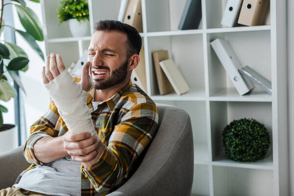 injured man suffering from pain and looking at hand in bandage 