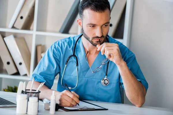 Zamyślony Lekarz Trzymający Długopis Pobliżu Schowka Klinice — Zdjęcie stockowe
